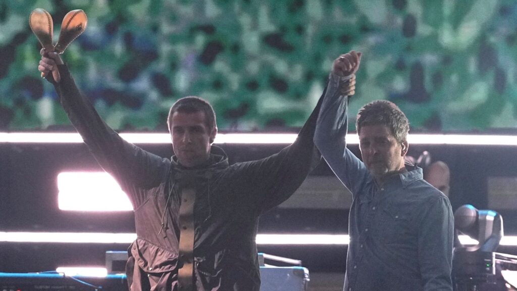 I fratelli Gallagher si danno il cinque e si abbracciano quando gli Oasis si riuniscono sul palco dopo 16 anni